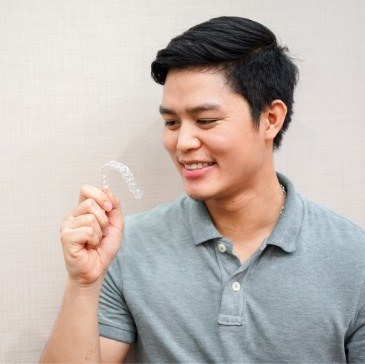 Man in gray polo shirt holding Invisalign clear aligner