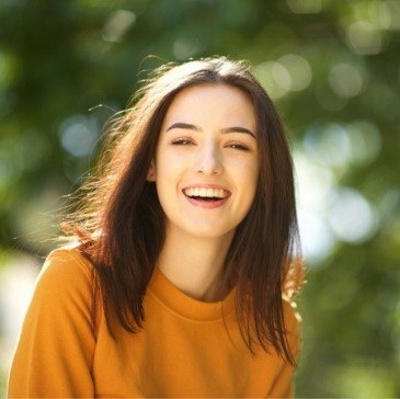 Young woman in orange shirt grinning outdoors