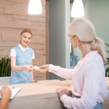 Dental patient handing dental insurance card to dental team member at front desk