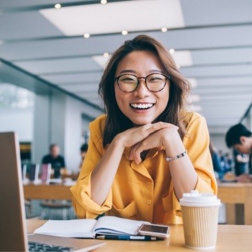 Smiling young woman sitting at desk in office with laptop