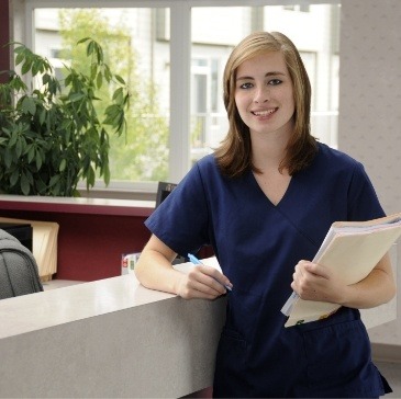 Smiling dental team member standing by front desk