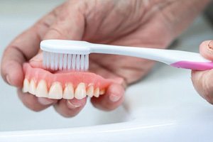 a person brushing their dentures over a sink