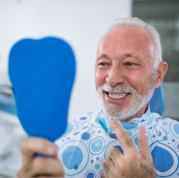 Senior dental patient admiring his smile in mirror