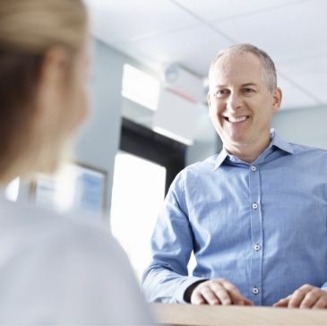 Man talking to front desk dental team member