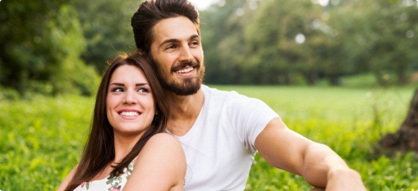Smiling man and woman sitting in grassy field