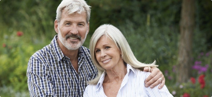 Senior man and woman smiling outdoors with implant dentures in Waco