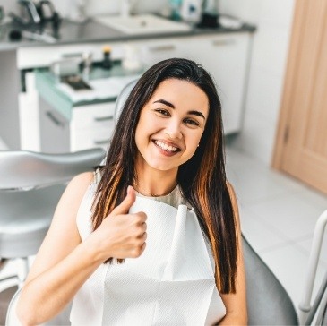 Smiling young woman giving thumbs up in dental chair