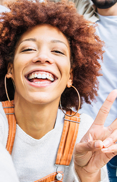 Smiling young woman with hoop earrings giving peace sign