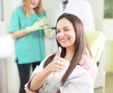Smiling young woman winking and giving thumbs up in dental chair