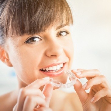 smiling woman holding Invisalign clear aligner
