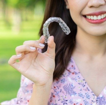 Woman holding Invisalign clear aligner outdoors