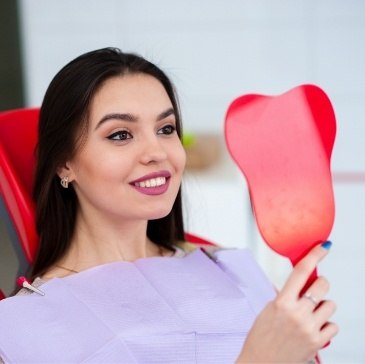 Young woman in dental chair admiring her smile in mirror