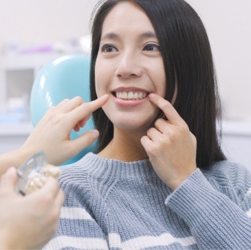 Dental patient in gray sweater pointing to her smile