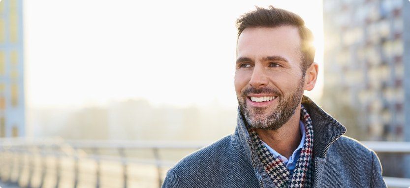 Man in peacoat smiling on city street after replacing missing teeth in Waco