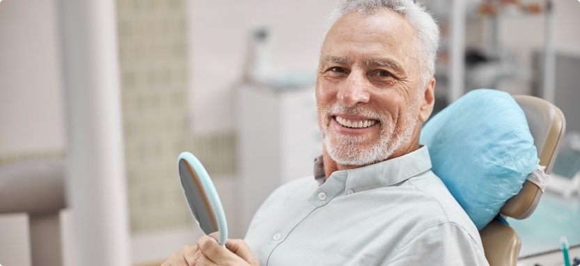 Senior man in dental chair holding mirror at Waco dental appointment