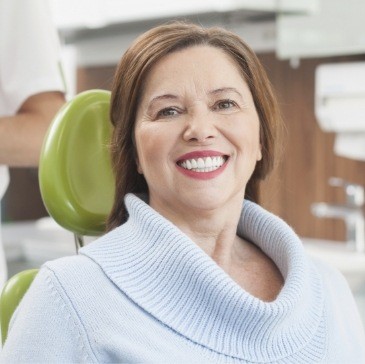Smiling senior woman in dental chair with light blue sweater