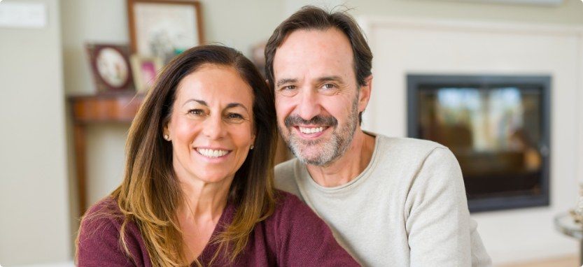 Man and woman in their living room smiling after restorative dentistry in Waco