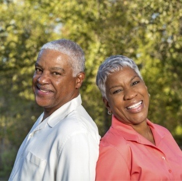 Senior man and woman smiling with trees in background