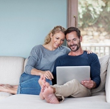 Man and woman sitting on couch looking at laptop