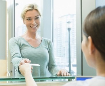 Dental patient handing dental team member a payment card at front desk