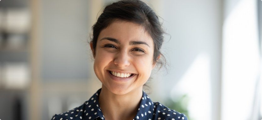 Woman in blue polka dot shirt smiling with dental veneers in Waco