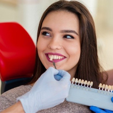 Cosmetic dentist holding a veneer to a patient's smile