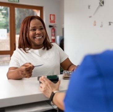 Woman handing payment card to dental team member at front desk