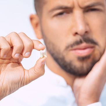 Man holding extracted tooth and touching swollen jaw in pain