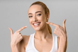 Woman pointing to her smile after getting same-day dental crowns