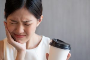 person drinking coffee and holding their mouth in pain