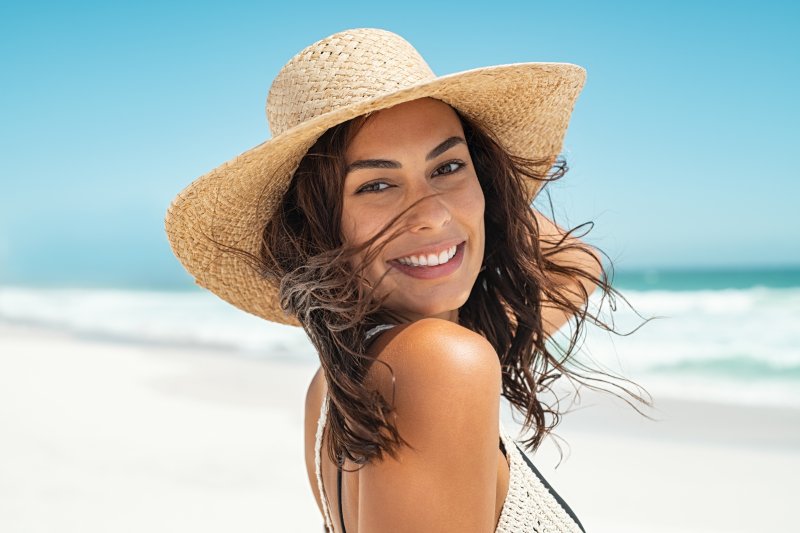 a young woman wearing a hat and smiling while on the beach 