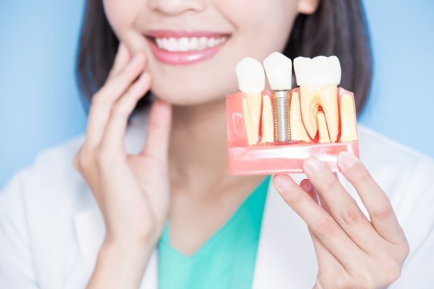 dentist smiling and holding dental implant model