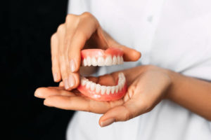 Close up of woman’s hands holding upper and lower denture