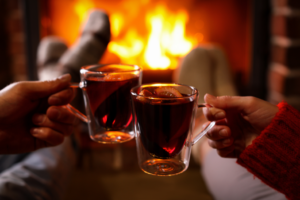 two people cheers-ing with mulled wine in front of a fireplace